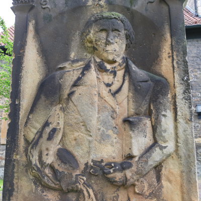 Relief eines Mannes mit Buch und Schlüssel auf dem Grabstein von Lehrer Wilhelm Adolf Thiesing auf dem Kirchhof in Oedelum