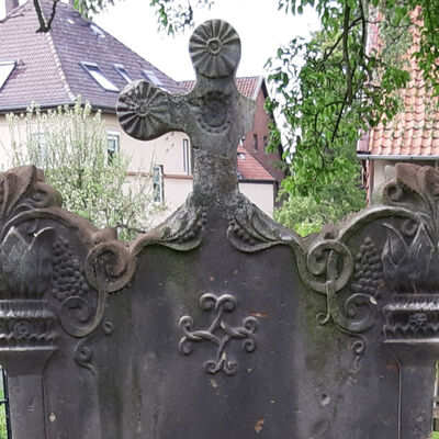 Auf dem Grabstein von Lehrer Thiesing auf dem Kirchhof in Oedelum sind Fackeln, Weintrauben und ein Ankerkreuz zu sehen.